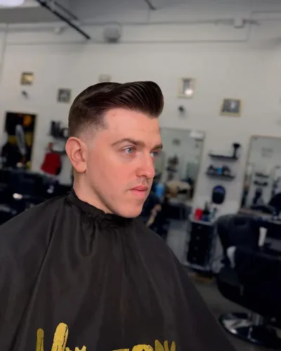 Side-part pompadour with a taper, finished in the shop&rsquo;s Victory cape